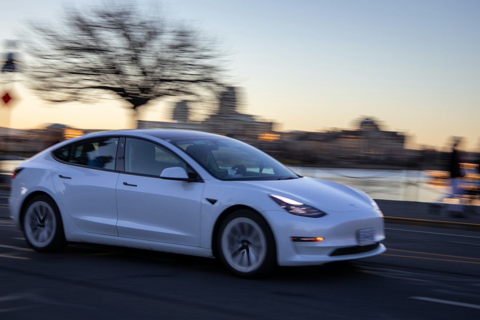 White electric sedan driving through a city at dusk